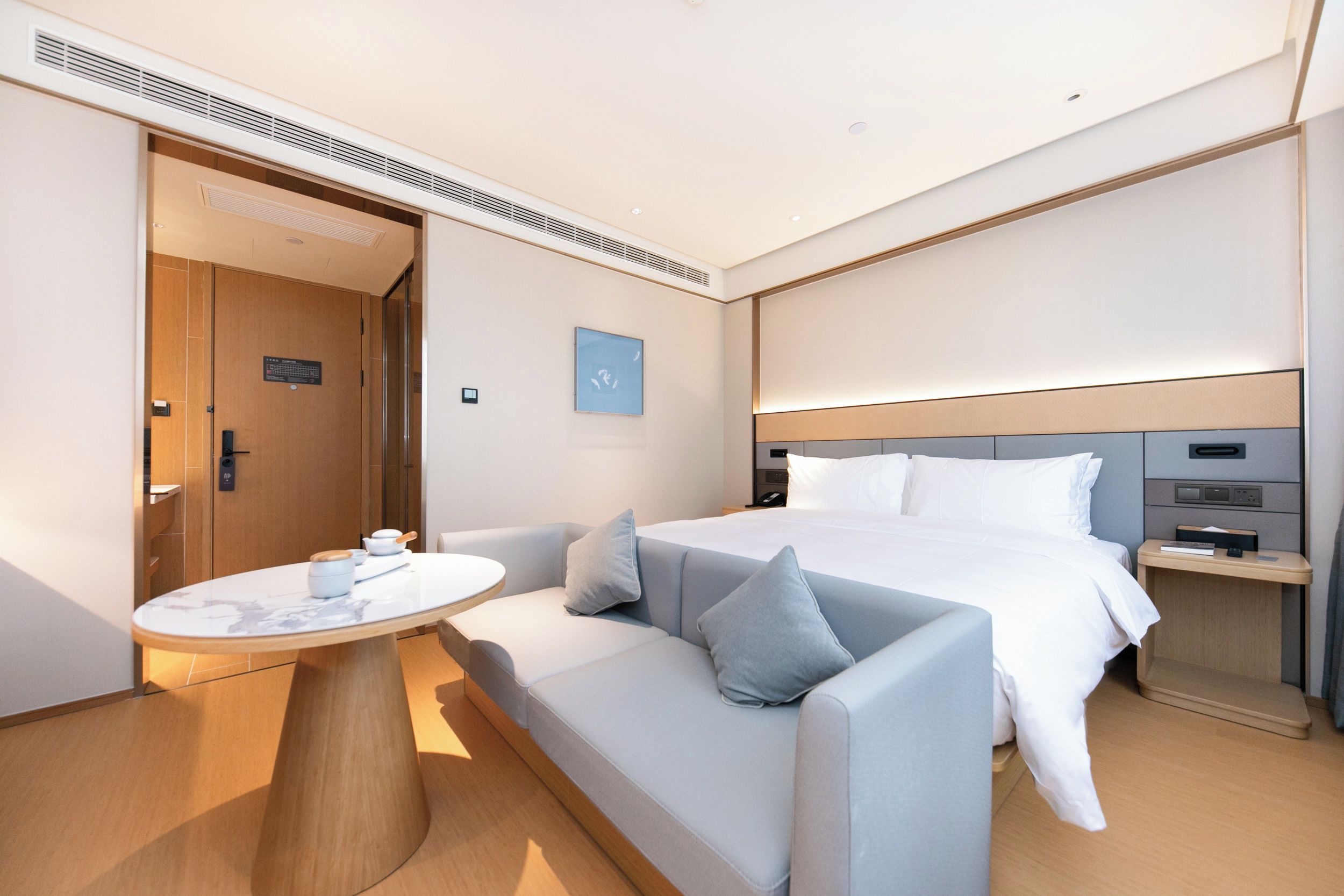 A modern hotel room with a bed, a sofa, a small table, and a bedside table.