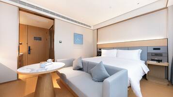 A modern hotel room with a bed, a sofa, a small table, and a bedside table.