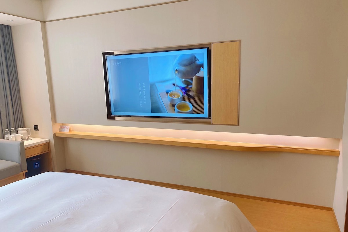 A hotel room with a bed, a desk with a computer, and a TV mounted on the wall.