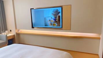 Een hotelkamer met een bed, een bureau met een computer en een aan de muur bevestigde televisie.
