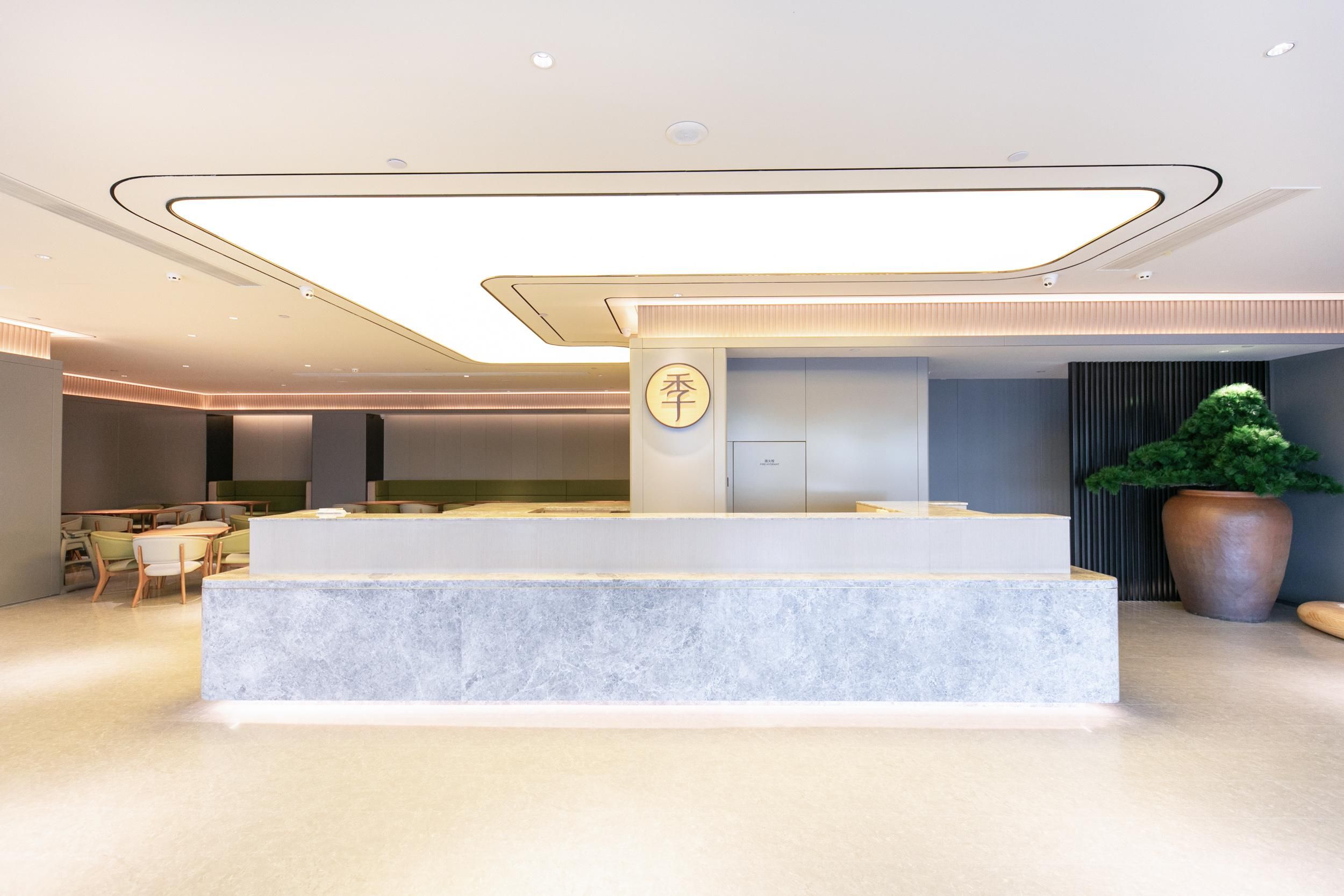 A modern reception area with a marble counter, seating area, and a large potted plant.