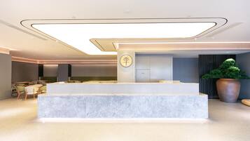 A modern reception area with a marble counter, seating area, and a large potted plant.