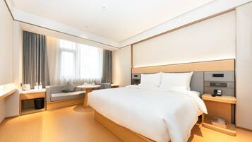 Een moderne hotelkamer met een groot bed, een bank, een kleine tafel en een nachtkastje met een lamp.