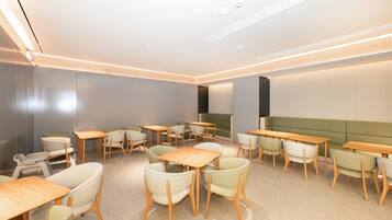 A modern dining area with wooden tables and chairs, a green sofa, and recessed ceiling lighting.