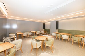 A modern dining area with wooden tables and chairs, a green sofa, and recessed ceiling lighting. - Ji Hotel (Xi'an)