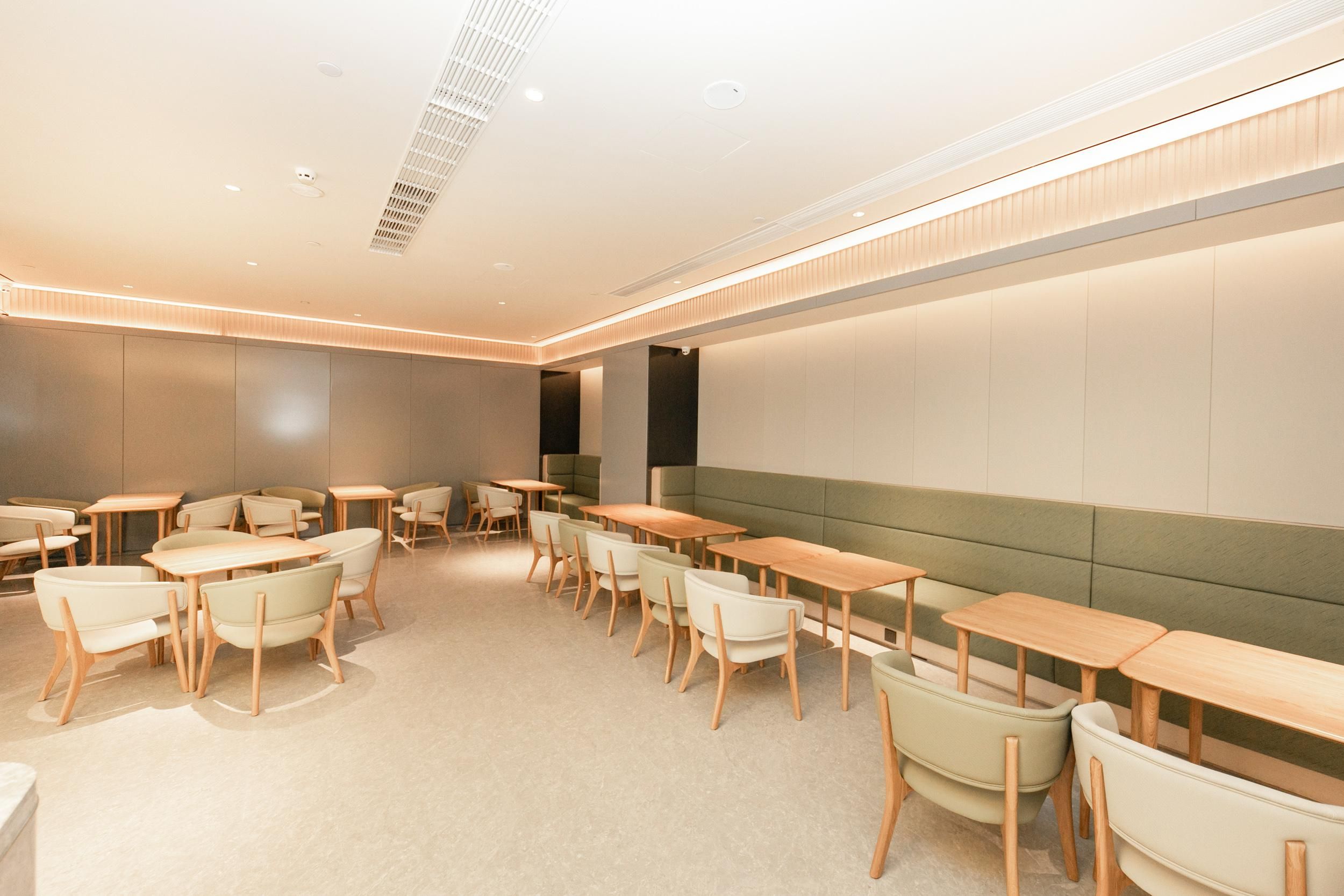 A modern dining area with wooden tables and chairs, a green cushioned bench, and recessed ceiling lighting.