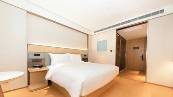 A modern hotel room with a large bed, bedside table, and a small desk.