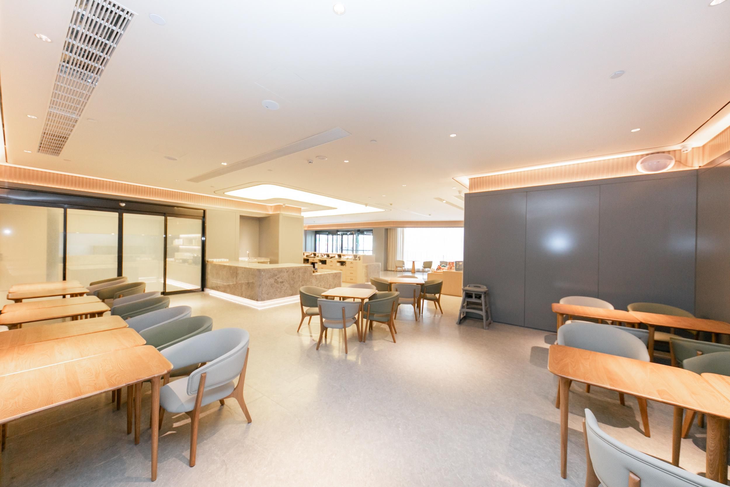 Un salón de conferencias moderno con mesas y sillas de madera, una isla central con un lavamanos y un amplio ventanal que proporciona luz natural.