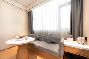 A modern hotel room with a sofa, a round table, and a bedside table with amenities. - Ji Hotel (Xi'an)