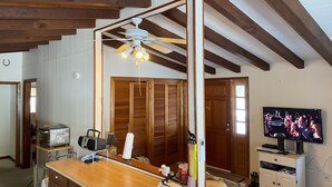 Una habitación con techo de madera, ventilador de techo, televisor y una zona de cocina con estufa, además de un sofá.
