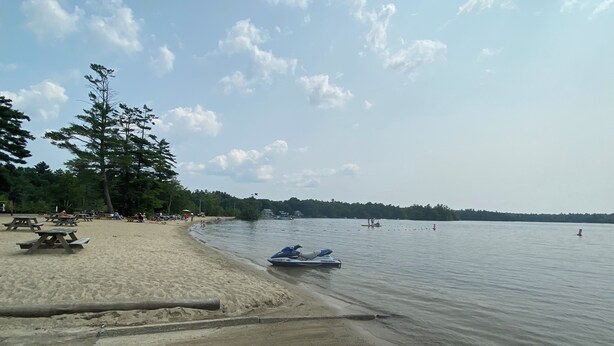 Una playa arenosa con mesas de picnic y un jet ski en el agua.
