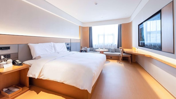 A hotel room with a large bed, bedside table with a phone, a desk with a chair, a sofa, and a large window. - Ji Hotel Nantong Motor East Station (Nantong)