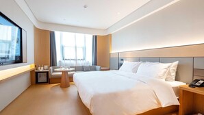 A hotel room with a large bed, a bedside table with a phone, a small round table with a lamp, a sofa, and a window with curtains. - Ji Hotel Nantong Motor East Station (Nantong)