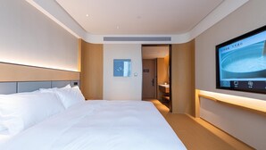 A hotel room with a large bed, a television mounted on the wall, and a door leading to a bathroom. - Ji Hotel Nantong Motor East Station (Nantong)