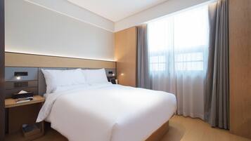Ein modernes Hotelzimmer mit einem großen Bett, Nachttischen, einem kleinen Tischchen, einem Fenster mit Vorhängen und einem Holzkopfende.