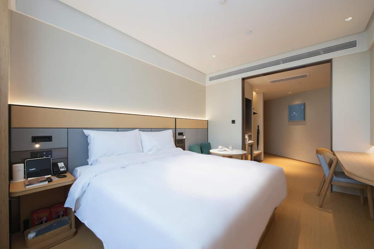 A hotel room with a bed, bedside table, lamp, and a small table with a chair.