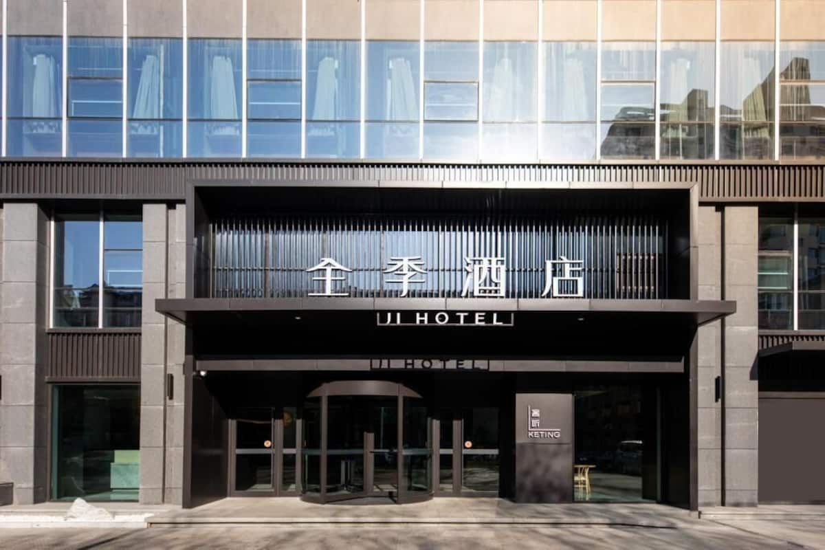 A modern hotel entrance with a glass facade, a sign reading 'JI HOTEL,' and a revolving door.