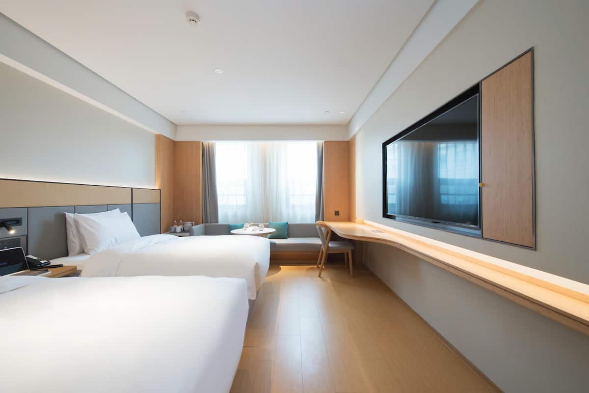A hotel room with two beds, a desk, a chair, a TV, and a window with curtains.