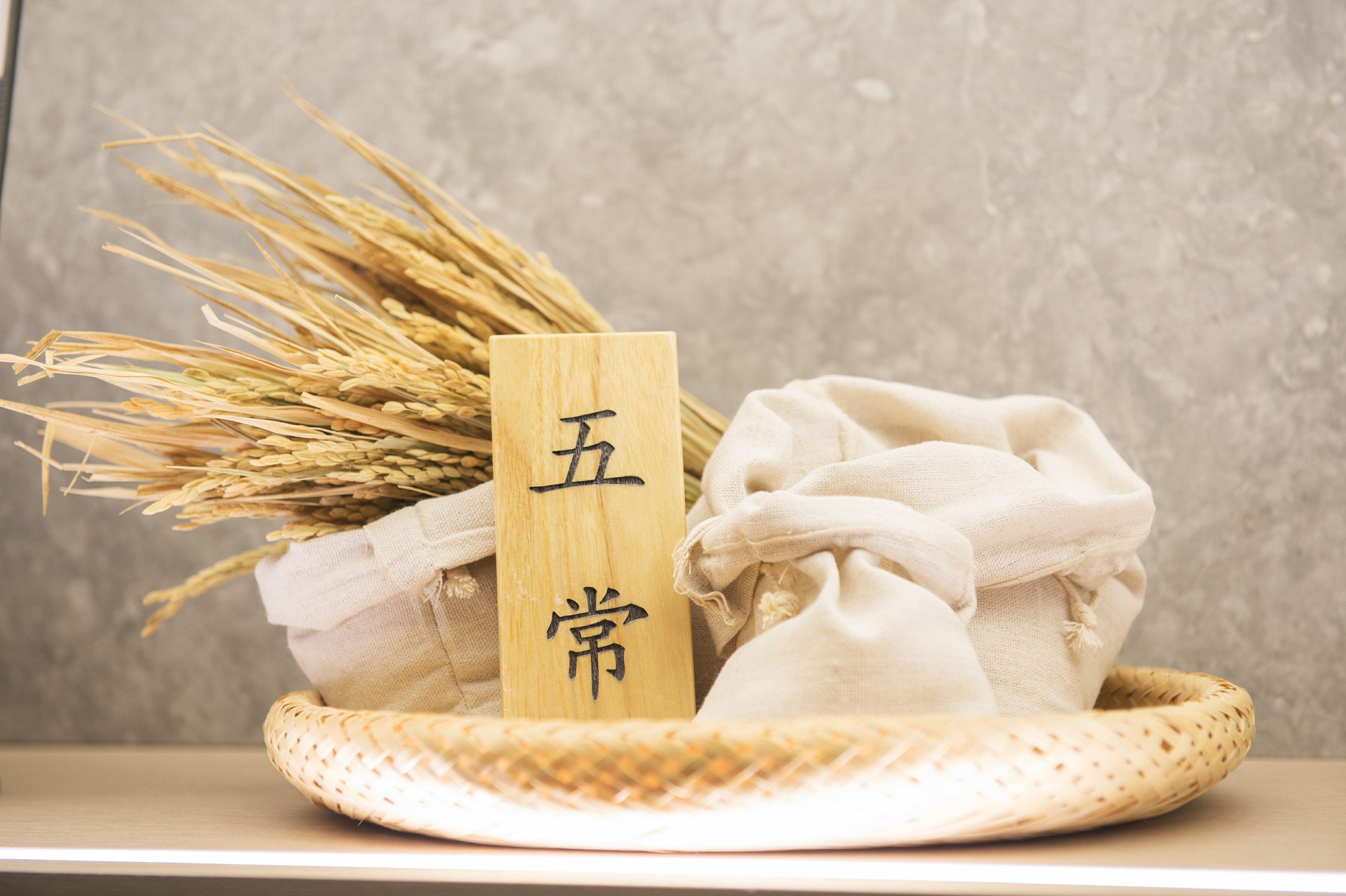A woven basket containing wheat, a wooden block with Chinese characters, and a cloth bag.