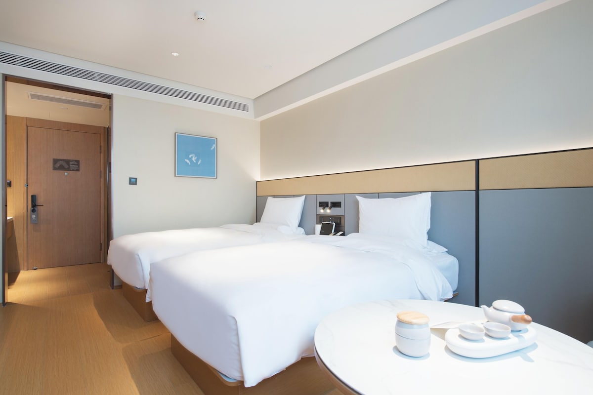 A hotel room with two beds, a round table with tea set, and a door with a sign.