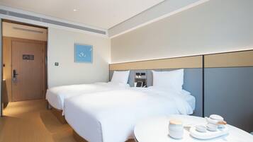 A hotel room with two beds, a round table with tea set, and a door with a sign.
