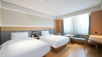A hotel room with two beds, a small table, a sofa, and a window with curtains.