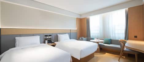 A hotel room with two beds, a small table, a sofa, and a window with curtains.