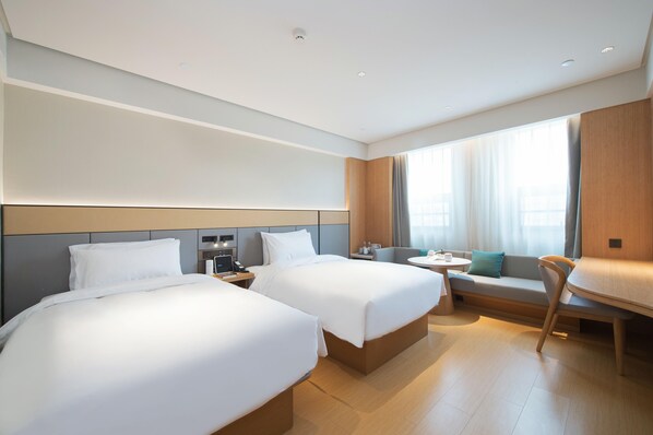 Una habitación de hotel con dos camas, una mesita pequeña, un sofá y una ventana con cortinas.