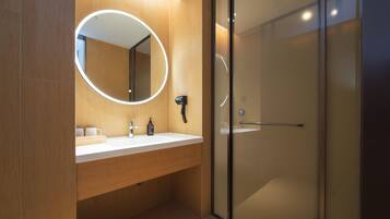 A modern bathroom with a wooden vanity, a round mirror with a light, and a glass shower enclosure.