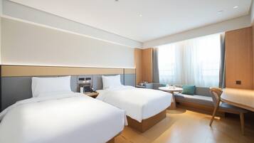 A hotel room with two beds, a small table, a sofa, and a large window with curtains.