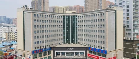 Un hôtel à plusieurs étages, doté d’une entrée principale et entouré de voitures garées et d’autres bâtiments.