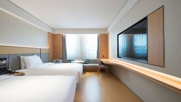 A hotel room with two beds, a desk, a chair, a TV, and a window with curtains.