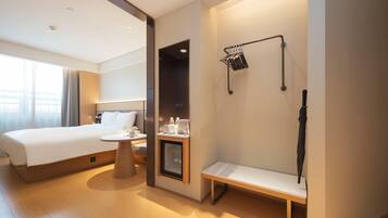 A hotel room with a bed, bedside table, bench, and a wall-mounted rack with items.