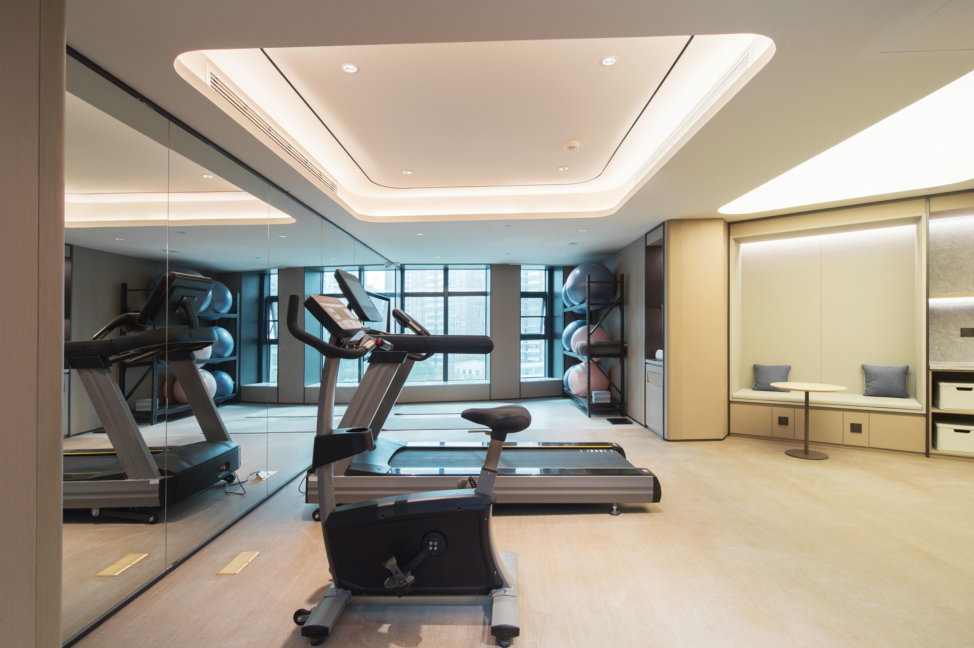 A modern gym with exercise equipment, large windows, and a seating area with a table.