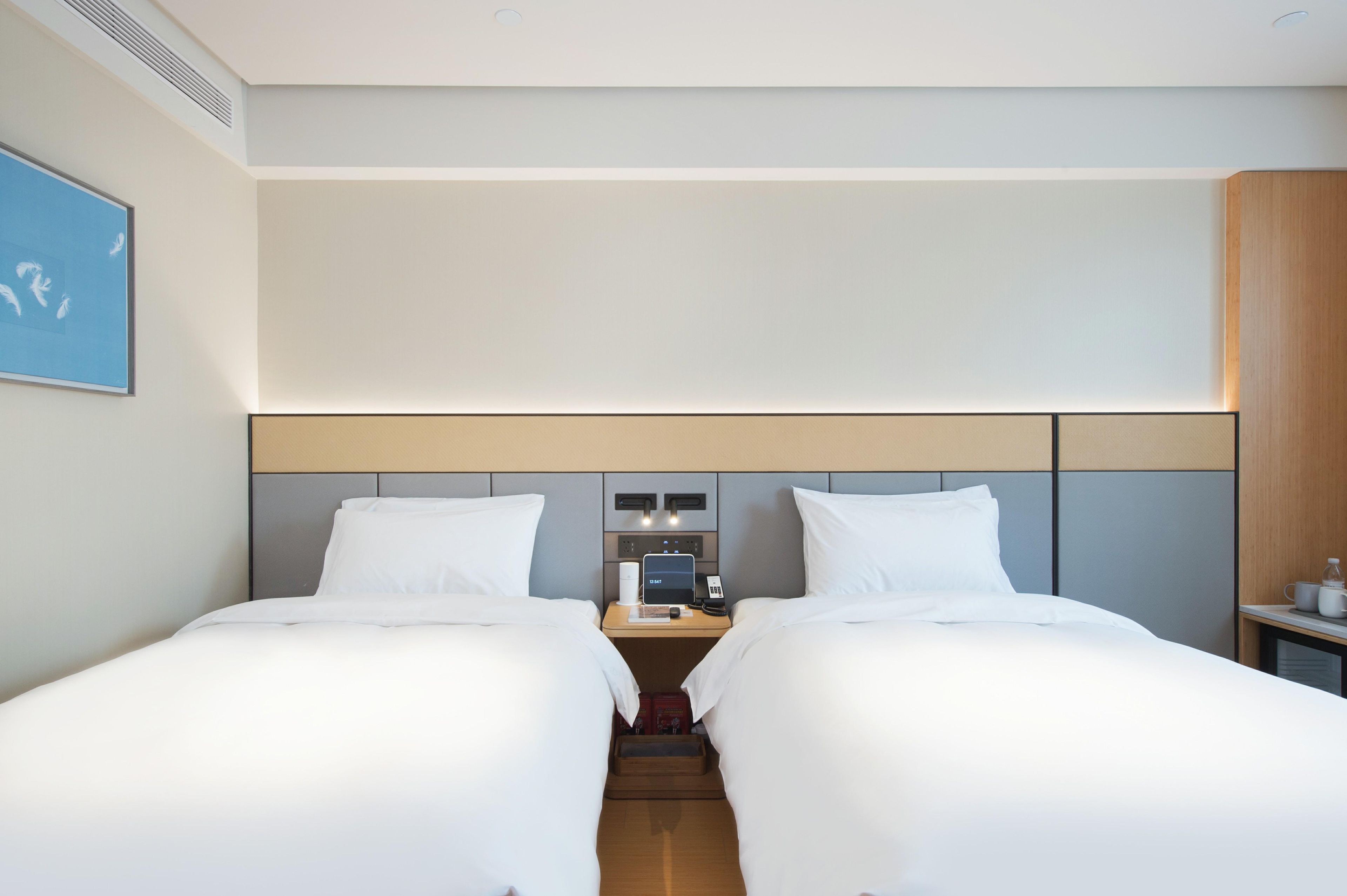 A hotel room with two beds, a nightstand with a phone and a laptop, and a wall-mounted light.