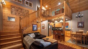 A spacious living area with a wooden staircase, a cozy seating area, a kitchen, and a dining space.