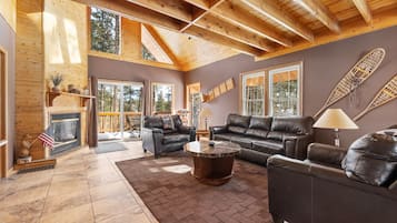 A spacious living room with a fireplace, leather sofas, and a large window overlooking a deck.