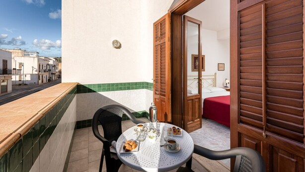 A balcony with a table set for breakfast, a chair, and a view of the street. - I Tre Golfi Corallo Apartment (San Vito Lo Capo)