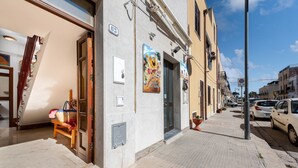 A street view with a building featuring a door, a bench, and a poster. - I Tre Golfi Corallo Apartment (San Vito Lo Capo)