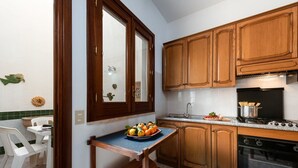 A compact kitchen with wooden cabinets, a built-in oven, and a small dining area with a table and chairs. - I Tre Golfi Corallo Apartment (San Vito Lo Capo)
