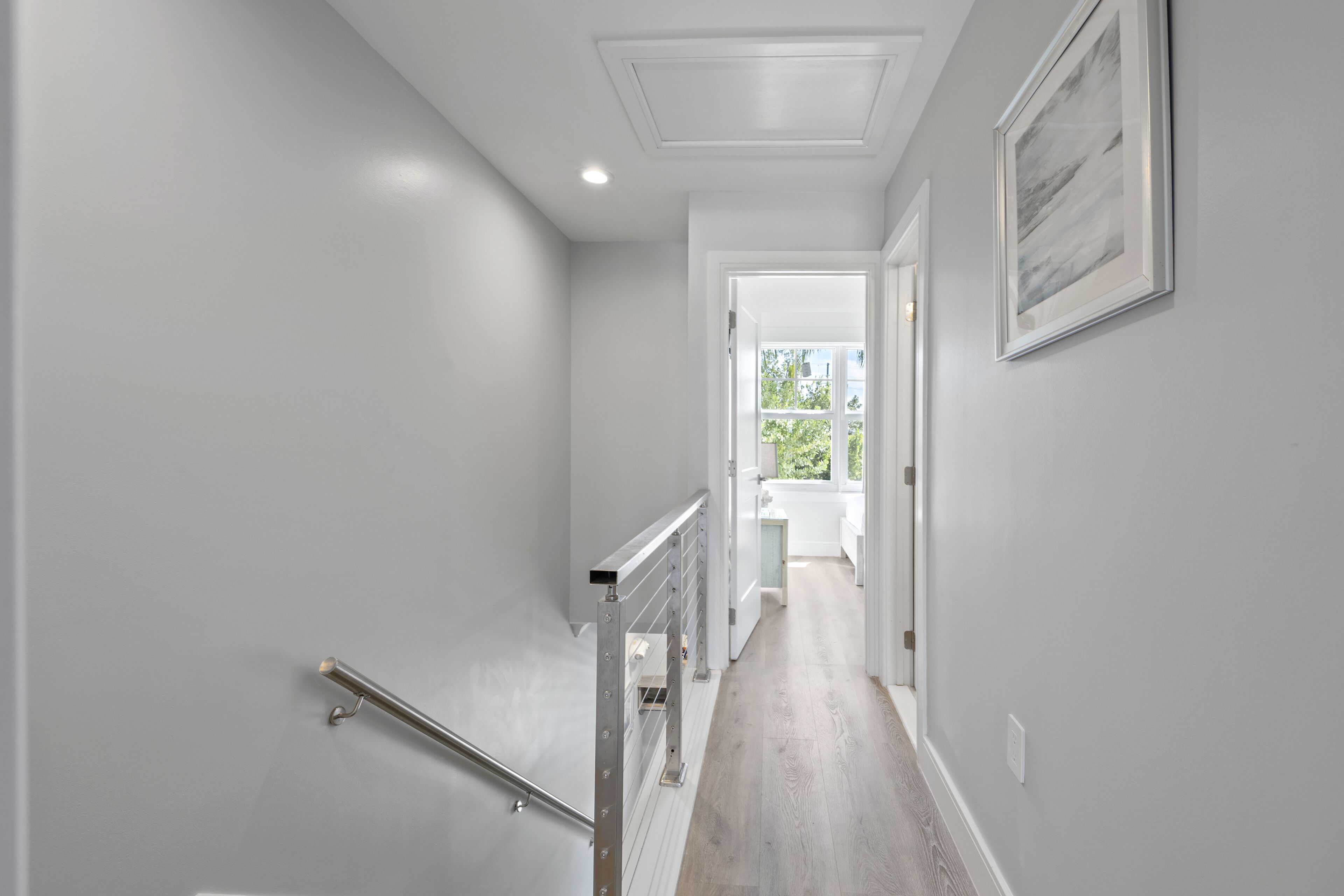 A hallway with a wooden floor, white walls, a metal handrail, and a framed picture on the wall.