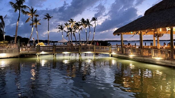 A waterfront resort with a wooden bridge, palm trees, and a thatched-roof pavilion. - Villa 5087 on Duck Key Boat Slip Available - 2BD 2.5BA (Duck Key)