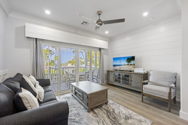 A spacious living room with a gray sofa, a wooden coffee table, and a TV on a wooden cabinet.