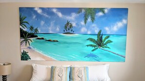 A bedroom with a bed, pillows, and a wall-mounted painting of a beach scene. - Oceanview Oasis⁘Private Heated Pool⁘Grill⁘Screened Porch⁘Beach Gear⁘Games (Fort Myers Beach)