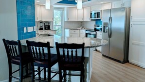 A modern kitchen with a central island, stainless steel appliances, and a blue accent wall. - Oceanview Oasis⁘Private Heated Pool⁘Grill⁘Screened Porch⁘Beach Gear⁘Games (Fort Myers Beach)