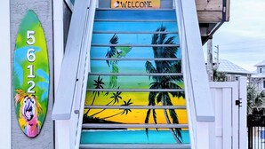 A staircase with a tropical mural, a 'WELCOME' sign, and a number sign. - Oceanview Oasis⁘Private Heated Pool⁘Grill⁘Screened Porch⁘Beach Gear⁘Games (Fort Myers Beach)