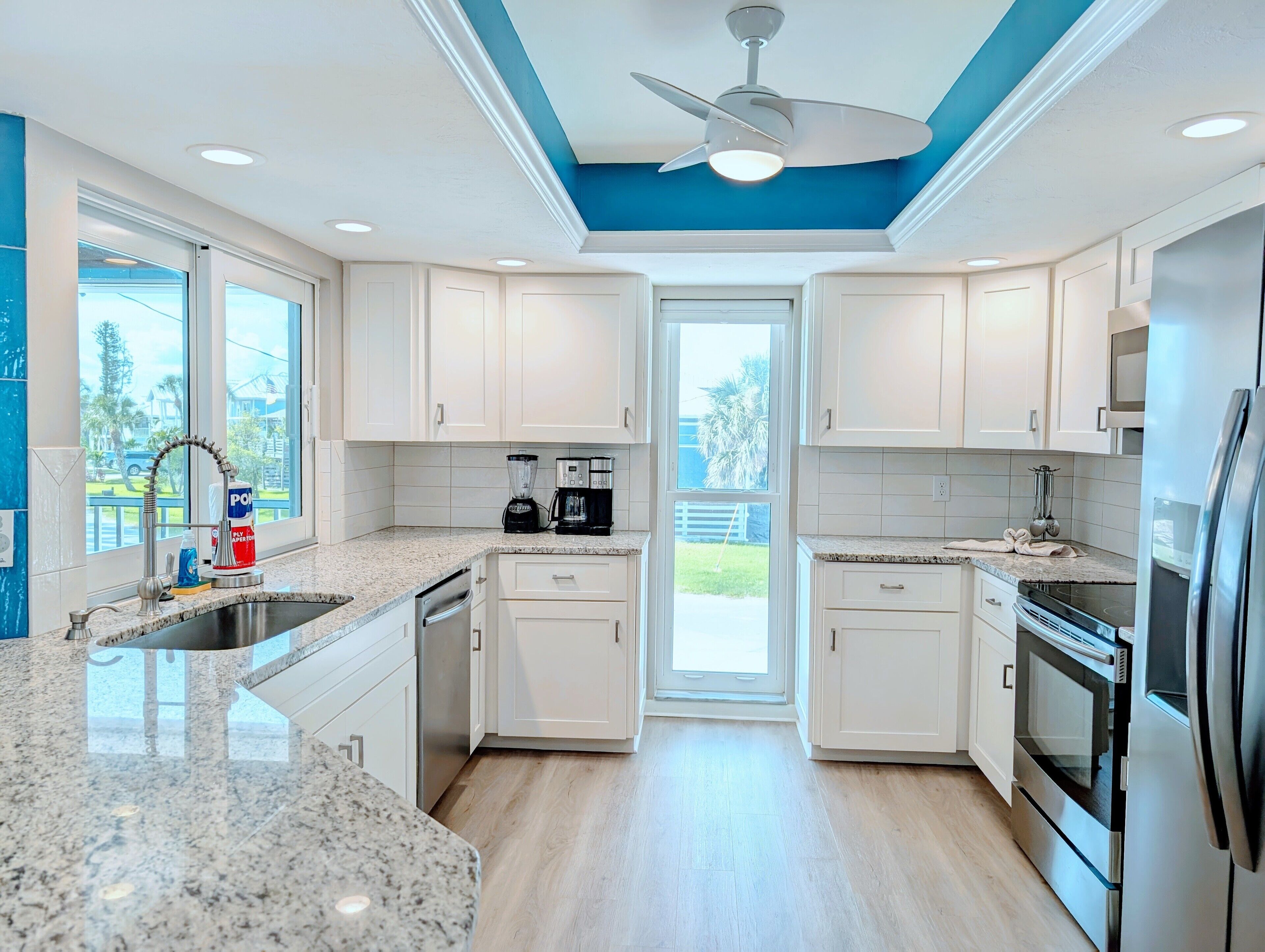 A modern kitchen with white cabinets, granite countertops, a built-in oven, and a ceiling fan.