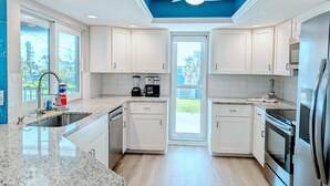 A modern kitchen with white cabinets, granite countertops, a built-in oven, and a ceiling fan. - Oceanview Oasis⁘Private Heated Pool⁘Grill⁘Screened Porch⁘Beach Gear⁘Games (Fort Myers Beach)