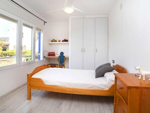 Een slaapkamer met een houten bed, een bureau met stoel, een kledingkast en een raam met uitzicht op groen.