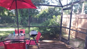 Une terrasse couverte avec une table et des chaises, un barbecue et un parasol rouge.